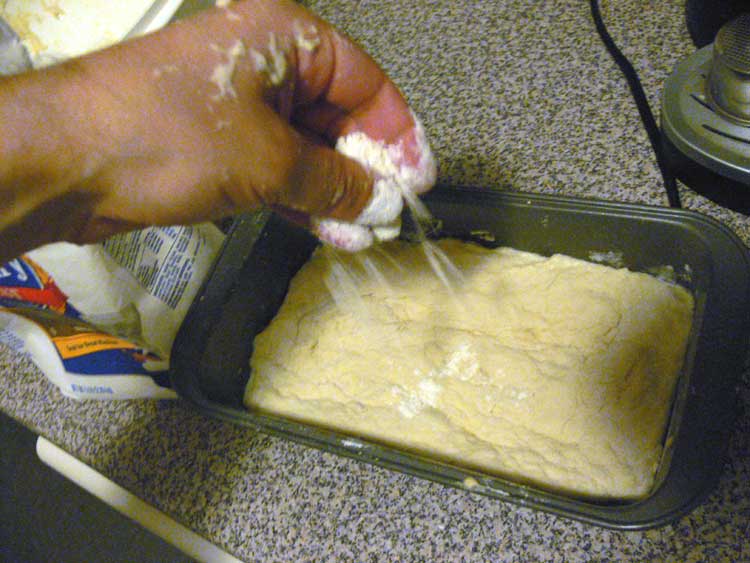 Sprinkling flour onto the top of bread paste in baking pans.